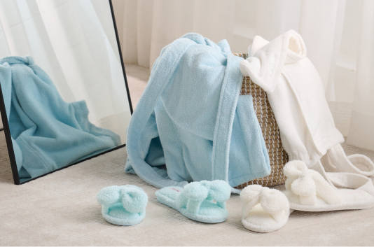 Two bathrobes in a basket, one white, the other blue, with matching slippers.